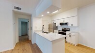 This single-floor space showcases a thoughtfully refreshed interior with a cohesive modern design carried consistently throughout. Light natural hardwood flooring runs seamlessly across every room, creating a warm and unified aesthetic that complements the crisp white walls and trim found throughout the home.

The kitchen serves as a central highlight, featuring a peninsula with striking quartz countertops accented by subtle grey veining and an undermount sink with a matte black faucet. White shaker-style cabinetry with black hardware lines the walls, complemented by a classic white subway tile backsplash. Stainless steel appliances — including a French door refrigerator, electric range, and over-the-range microwave — complete the functional and polished look. Recessed lighting adds a bright, clean finish overhead. A dedicated dining area adjacent to the kitchen provides additional space for everyday living.

The open living area is spacious and airy, enhanced by crown molding, a ceiling fan with light fixture, and a large window that invites natural light and outdoor greenery views. The bedrooms are generously proportioned, each with neutral white walls, hardwood flooring, and windows offering natural light. The bathroom maintains the same clean design language, with a white vanity, black hardware accents, a full tub-shower combo, and continued hardwood-style flooring.