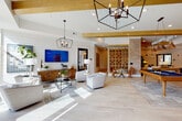 This single-floor amenity space is a thoughtfully designed communal environment that seamlessly blends coastal-inspired aesthetics with contemporary sophistication. The architecture is defined by white shiplap ceilings accented with bold gold-painted wood beams, light wood-look tile flooring, and an open layout that connects multiple distinct zones while maintaining a cohesive visual identity throughout.

The main lounge area features an abundance of natural light, geometric black iron pendant chandeliers, and a curated seating arrangement of neutral upholstered chairs surrounding a central coffee table. A decorative lattice partition and stacked stone accent wall serve as architectural focal points, framing a secondary lounge with warm-toned sofas, a bold stone feature wall, and a mounted flat-screen television.

A game room with a pool table adds a recreational element, while a dedicated dining area offers a long communal table with woven rattan seating beneath pendant lighting, complemented by built-in cabinetry, a wet bar sink, and wall-mounted televisions.

A separate lounge wing with teal velvet furnishings, a beaded chandelier, and black-framed glass partition doors leads to private meeting or conference rooms. A compact wet bar kitchenette with teal subway tile, marble countertops, and mounted screens completes the versatile layout.