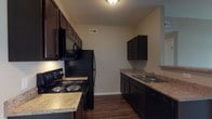 Located at 7086 Crown Lake Dr in Reynoldsburg, Ohio, this single-floor residence offers a well-designed, open layout that connects the main living areas with functional ease. The kitchen is outfitted with rich dark espresso cabinetry, granite-style countertops, and a full suite of black appliances including an electric range, over-the-range microwave, refrigerator, and dishwasher. Durable wood-style flooring anchors the kitchen space, providing a sleek contrast to the cabinetry. A peninsula with a pendant light overhead creates a natural transition into the open living and dining area, which features neutral-toned plush carpeting and warm, soft wall colors throughout. The living area is generously proportioned, with a set of French doors that invite natural light and provide access to an outdoor space, enhancing the overall sense of openness. A coat closet near the main entry adds practical storage. The bathroom features tile flooring in a stone-like pattern, a dark vanity with a granite-style countertop, and a full tub-shower combination with clean white surrounds. Neutral paint tones, consistent finishes, and a straightforward single-level floor plan make this a comfortable and easy-to-navigate residence in the Crown Lake community of Reynoldsburg.