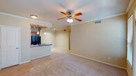 Located at The Lakes At Cypresswood in Houston, TX 77070, this single-floor residence offers a well-organized layout with comfortable living spaces throughout. The open-concept living area is finished with plush carpeting and crown molding, and is anchored by a ceiling fan with light fixture. The space flows seamlessly into the kitchen, which features a raised breakfast bar peninsula, dark granite-style countertops, warm wood cabinetry, black appliances including a side-by-side refrigerator, electric range, and built-in microwave, all set atop light tile flooring with track and pendant lighting above. The front entry opens into the living area, which includes access to an outdoor balcony through a windowed door, allowing natural light to filter in. The bedrooms are generously sized with soft carpeting and ceiling fans, and one room includes built-in shelving and a desk surface alongside a large window with tree-lined views. The bathroom is finished with neutral tile flooring, a full soaking tub with a tiled surround, and dark granite countertops at the vanity. Throughout the residence, warm beige tones and consistent finishes create a cohesive and comfortable living environment.