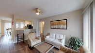 This single-floor unit offers a thoughtfully laid-out living space with a warm, neutral color palette and wood-look flooring throughout. The open-concept living room serves as the heart of the home, featuring a tufted white loveseat, patterned accent chairs, and a framed landscape artwork on the wall. A sliding glass door in the adjacent dining area floods the space with natural light and provides access to an outdoor balcony, where a round bar-height dining table with four chairs creates an inviting spot for meals. The galley-style kitchen is efficiently designed with white cabinetry, tile backsplash, light countertops, and black appliances including a refrigerator and gas range. Two bedrooms offer comfortable retreats, each with wood-look flooring, windows with blinds allowing ample natural light, and white dresser storage. The bathroom features a full soaking tub with a tile surround accented by a decorative mosaic border, offering a clean and classic finish. Throughout the unit, the consistent warm beige tones and natural light create a cohesive and welcoming atmosphere well-suited for everyday living.