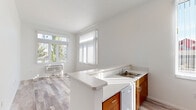 Located in Beaverton, Oregon, this single-floor, 3-bedroom, 1-bathroom home offers a clean, modern design with a bright and functional layout. The kitchen is a standout feature, boasting warm wood-toned cabinetry, light countertops, a peninsula with an integrated sink, a dishwasher, electric range, and a full-size refrigerator. Tall ceilings and a narrow vertical window allow natural light to fill the space, while light wood-style flooring extends throughout the main living and kitchen areas. The living area adjoins the kitchen and is bathed in sunlight through large windows dressed with vertical blinds, offering pleasant outdoor views of the surrounding neighborhood. The primary bedroom is generously proportioned, featuring soaring ceilings, soft carpet flooring, and a reach-in closet with shelving. The additional bedrooms also feature carpet flooring, individual closets, and windows that bring in natural light. The shared bathroom is well-appointed with a full tub and shower combination, a single-sink vanity with a mirror, and warm wood-tone cabinetry, complemented by wood-style flooring. Clean white walls and consistent finishes throughout give the home a cohesive, contemporary feel.