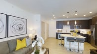 Located at 6963 E 109th Ave in Westminster, Colorado, this single-floor residence offers a thoughtfully designed open-concept layout that seamlessly integrates the living and kitchen areas. The living space features light hardwood-style flooring, recessed lighting, and clean white walls that lend a bright, airy atmosphere. A comfortable seating area anchors the living room, complemented by tasteful décor including bold accent pieces and framed wall art.

The kitchen is a standout feature, showcasing dark charcoal cabinetry that contrasts elegantly with light countertops and a crisp white backsplash. Stainless steel appliances add a modern touch, while pendant lighting suspended above the breakfast bar creates a warm, inviting focal point. The bar-height counter with contemporary seating provides a casual dining option and serves as a natural divider between the kitchen and living areas.

The overall ambiance is modern and cohesive, with a neutral color palette punctuated by vibrant yellow accents. Recessed lighting throughout ensures consistent illumination across the open floor plan. The interior exudes a clean, contemporary aesthetic that balances both functionality and style, making it an appealing and well-appointed single-level living space.