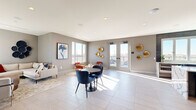This single-floor space is a well-appointed lounge or amenity room that seamlessly connects indoor and outdoor living through a set of glass-paned French doors leading to an expansive rooftop terrace. The interior is finished with large-format, light-toned porcelain tile flooring that reflects natural sunlight streaming in from multiple windows, creating a bright and airy atmosphere throughout.

The interior design is contemporary and curated, featuring warm greige walls accented by decorative gold disc wall art and vibrant framed artwork. Seating areas are thoughtfully arranged with a mix of a neutral sofa, navy blue velvet chairs around a round pedestal table, and accent chairs in bold red tones. A wet bar area is anchored by a striking dark wood-paneled accent wall and a marble-topped counter, adding a refined, upscale touch. Recessed lighting supplements the abundant natural light overhead.

The rooftop terrace extends the space considerably, offering expansive city skyline views and furnished with woven lounge chairs, sectional seating, and a covered pergola area with a ceiling fan—ideal for outdoor gatherings. Glass railings preserve unobstructed sightlines across the surrounding urban landscape, reinforcing the elevated, modern character of this versatile space.