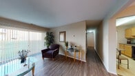 Located at 2010 Pinehurst Ct in Allentown, PA, this single-floor residence offers a thoughtfully laid-out living space with a clean, neutral aesthetic throughout. The living room is a welcoming area featuring rich hardwood-style flooring, a large sliding glass door dressed with vertical blinds that floods the space with natural light and provides views of the outdoor greenery. A hallway connects the main living areas seamlessly to the private rooms. The kitchen is efficiently designed with light wood cabinetry, granite-style countertops, tile flooring, and black appliances including a gas range, dishwasher, and over-the-range microwave. Adjacent to the kitchen, the dining room offers a warm gathering space highlighted by a chandelier, hardwood-style floors, and a bold accent wall. The primary bedroom features plush carpeting, ample natural light from a window with vertical blinds, and access to a closet. A second bedroom provides similar comfort with soft carpet and bright windows. The bathroom is well-appointed with a white vanity, medicine cabinet mirror with overhead lighting, and tile flooring. Overall, the space presents a comfortable and functional layout well-suited for everyday living.