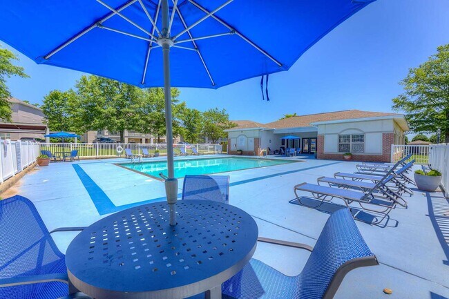 Piscina al aire libre con mesas y sillas a la sombra, tumbonas y un edificio de casa club rodeado de árboles y una terraza vallada. - Parham Pointe