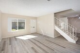 Located at 2002 E Santa Clara Ave in Santa Ana, CA, this two-story, 2-bedroom, 2-bathroom home offers a thoughtfully laid-out floor plan spread across two evenly sized floors. The main level features a bright entryway with a front window that floods the space with natural light, opening to a generous living room finished with light-toned hardwood-style flooring. A standout white brick fireplace anchors the living room, which also includes sliding glass doors leading directly to a private patio. An adjacent dining area connects seamlessly to the kitchen, which is outfitted with white cabinetry, white quartz-style countertops, a full suite of appliances, and a window above the sink providing natural light. A decorative staircase with an ornate railing leads to the upper floor, where both bedrooms are located. The bedrooms feature neutral carpet, windows with outdoor views of surrounding greenery, and dedicated closets. The primary bedroom includes an en-suite bathroom and a walk-in closet. Both bathrooms are finished with light hardwood-style flooring, vanities with stone-look countertops, and built-in shelving for storage. A stacked washer and dryer unit is conveniently housed within the home. Warm neutral tones and textured ceilings carry throughout, creating a cohesive and comfortable living environment.