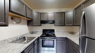 Located at 1200 Vineyard Dr in Broadview Heights, Ohio, this single-floor residence offers a well-organized layout with distinct living, kitchen, bedroom, and bathroom areas. The kitchen is equipped with rich gray cabinetry featuring raised-panel doors, light granite-style countertops, a stainless steel range with an overhead ventilation hood, a stainless steel refrigerator, and a single-basin sink. The floor is finished with large-format marble-look tile, adding a clean, polished feel to the space. The open living area is carpeted and features a large window with vertical blinds that invites natural light into the room, creating a bright and welcoming atmosphere. A hallway connects the living space to the bedroom, which is also carpeted and notably features two separate closets — one a walk-in style with built-in shelving and another with additional shelving — offering generous storage capacity. The bathroom is clean and functional, appointed with white tile surrounding the full tub-shower combination, a white vanity with a mirrored medicine cabinet above, and marble-look tile flooring consistent with the kitchen. The entry foyer features hard flooring, providing a practical transition zone. Overall, the space presents a tidy, move-in ready layout suited for comfortable everyday living.