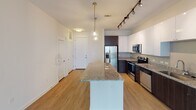 Located at 400 Faison Ave in Charlotte's vibrant 28205 corridor, this single-floor residence offers a thoughtfully designed layout with modern finishes throughout. The open-concept kitchen is a standout feature, showcasing sleek white upper cabinetry paired with dark wood lower cabinets, granite countertops, and a full suite of stainless steel appliances including a refrigerator, range, microwave, and dishwasher. A large granite-topped kitchen island anchors the space and doubles as a breakfast bar, illuminated by elegant pendant lighting and complemented by directional track lighting overhead. Light wood-style flooring flows through the kitchen and living areas, creating a warm, cohesive aesthetic. The living area benefits from a floor-to-ceiling sliding glass door fitted with vertical blinds, allowing abundant natural light and providing access to an outdoor view of the surrounding neighborhood. The bedroom is carpeted for comfort and features dual windows that bring in additional daylight, along with a ceiling fan for year-round climate control. A walk-in closet with wire shelving offers generous storage. The bathroom is finished with a dark wood vanity, granite countertop, framed mirror, and light wood flooring, with a direct entry into the walk-in closet. The overall ambiance is clean, contemporary, and move-in ready.