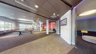 Located in West Palm Beach, Florida, this dynamic single-floor recreational facility offers an exciting and well-appointed amenity experience. The space is defined by bold, vibrant design choices, including striking red accent walls emblazoned with bold bowling-themed typography such as "Strike," "Cranker," and "King Pin," creating an energetic atmosphere throughout.

The bowling area features polished hardwood lanes visible through floor-to-ceiling glass partitions, with plush curved seating upholstered in deep plum velvet positioned alongside for spectators. Adjacent to the lanes, a lively game room offers a pool table and foosball table as centerpieces, illuminated by large pendant light fixtures. Generous windows along the perimeter flood this area with natural light and provide views of the surrounding palm-lined outdoor environment.

A dedicated karaoke lounge sets a more intimate tone, featuring ambient purple LED cove lighting, a large wall-mounted television, and comfortable curved seating. A circular lounge room with a domed ceiling, purple accent lighting, and a wraparound curved sofa creates an inviting social hub. Throughout the space, neutral carpet flooring, recessed lighting, and a refined dark drop ceiling provide a polished, cohesive backdrop to the vibrant recreational programming.