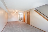 This two-floor residence offers a straightforward and functional layout designed for comfortable everyday living. The main level features an open living area finished with neutral-toned carpet and a ceiling fan with light fixture, providing a welcoming atmosphere. A staircase with a wooden handrail connects the two floors, and multiple interior doors lead to additional spaces including closets and utility areas. The kitchen is equipped with wood-toned cabinetry, a black refrigerator, a gas range, a sink, and wood-look vinyl flooring, creating a clean and practical cooking space.

The upper level hosts the bedrooms, each carpeted and finished with neutral walls and wood trim baseboards. One bedroom features mirrored sliding closet doors, while others offer standard door closets. A textured ceiling is consistent throughout the home, adding a classic residential finish. The full bathroom includes a tub-shower combination with a chrome curtain rod, a toilet, and a vanity with a countertop, all set against warm taupe walls and wood-look flooring. Windows throughout the home allow natural light to filter in, enhancing the overall brightness and livability of the space.