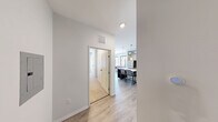 Located at 1107 S University Ave in the heart of Ann Arbor, Michigan, this 4-bedroom, 5-bathroom unit offers a modern, urban living experience with a distinctive industrial aesthetic. Exposed silver ductwork runs throughout the space, complementing the clean white walls and light wood-style flooring found in the main living areas.

The combined kitchen and living room serves as the social hub of the unit. The kitchen features dark espresso cabinetry, stainless steel appliances including a refrigerator, range, and microwave, granite-style countertops, and a large white island with seating — all illuminated by stylish pendant lighting. The living area is bathed in natural light from floor-to-ceiling windows that offer views of the surrounding Ann Arbor cityscape, creating an open, airy atmosphere.

Each of the four bedrooms is a private, functional space with individual windows providing natural light and urban views. The bedrooms are efficiently laid out and offer comfortable accommodations. Five bathrooms serve the unit, each featuring clean white walk-in showers with brushed nickel fixtures, dark wood vanities with granite-topped sinks, and wood-look flooring. A connecting hallway links the bedrooms and bathrooms, ensuring a practical flow throughout the unit.
