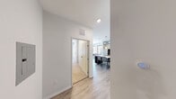 Located at 1107 S University Ave in the heart of Ann Arbor, Michigan, this 4-bedroom, 5-bathroom unit offers a modern, urban living experience with a distinctive industrial aesthetic. Exposed silver ductwork runs throughout the space, complementing the clean white walls and light wood-style flooring found in the main living areas.

The combined kitchen and living room serves as the social hub of the unit. The kitchen features dark espresso cabinetry, stainless steel appliances including a refrigerator, range, and microwave, granite-style countertops, and a large white island with seating — all illuminated by stylish pendant lighting. The living area is bathed in natural light from floor-to-ceiling windows that offer views of the surrounding Ann Arbor cityscape, creating an open, airy atmosphere.

Each of the four bedrooms is a private, functional space with individual windows providing natural light and urban views. The bedrooms are efficiently laid out and offer comfortable accommodations. Five bathrooms serve the unit, each featuring clean white walk-in showers with brushed nickel fixtures, dark wood vanities with granite-topped sinks, and wood-look flooring. A connecting hallway links the bedrooms and bathrooms, ensuring a practical flow throughout the unit.