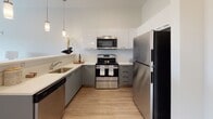 Located at 72 Elliot Ave in Quincy, Massachusetts, this single-floor unit presents a thoughtfully designed, modern interior with a cohesive open-concept layout. The living area features light hardwood-style flooring, neutral walls, and large windows that invite natural light, creating a bright and welcoming atmosphere. A comfortable seating area flows seamlessly into the dining and kitchen space, making the layout well-suited for both everyday living and entertaining.

The kitchen is a standout feature, equipped with stainless steel appliances including a refrigerator, range, microwave, and dishwasher. Sleek white upper cabinetry contrasts with gray lower cabinets, while light quartz-style countertops and pendant lighting add a polished, contemporary feel. A breakfast bar with seating for three provides a casual dining option adjacent to the kitchen.

The bedroom is a calm, carpeted retreat with neutral tones, a large window offering outdoor views, and access to a closet. The space is well-proportioned and filled with natural light. The bathroom features a clean, all-white tub and shower surround with chrome fixtures, maintaining the unit's consistent modern aesthetic throughout.