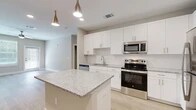 Located at 350 Bay Laurel Dr in Saint Augustine, FL, this single-story, 3-bedroom, 2-bathroom home offers a well-designed layout with modern finishes throughout. The open-concept kitchen and living area serves as the heart of the home, showcasing crisp white shaker cabinetry, a subway tile backsplash, granite countertops, and a central island with pendant lighting overhead. Stainless steel appliances — including a range, built-in microwave, dishwasher, and refrigerator — complete the kitchen. Light wood-look flooring runs through the main living areas, adding warmth and continuity. The three bedrooms feature plush carpeting, ceiling fans, and windows that invite natural light. The spacious primary bedroom includes a walk-in closet with wire shelving for organized storage. Both bathrooms are finished with granite-top vanities, white cabinetry, and tile-surround tub-shower combinations set on wood-look flooring. A dedicated laundry room houses a full-size top-load washer and dryer. Neutral wall tones and clean white trim throughout create a bright, cohesive aesthetic, making this home a functional and comfortable residence in the Saint Augustine area.