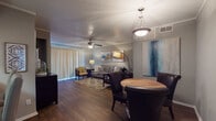 This single-floor residence offers a thoughtfully designed layout that seamlessly connects the main living areas. The open-plan living and dining space is anchored by rich hardwood-style flooring, a textured ceiling, and ceiling fans that add both function and character. A large sliding glass door floods the living room with natural light, while a pendant light fixture defines the dining area, which comfortably accommodates a round table and chairs. The living room features crown molding and a cozy seating arrangement centered around a glass coffee table and area rug.

The galley-style kitchen is well-equipped, showcasing white cabinetry, granite countertops, a mosaic tile backsplash, and black appliances. A pass-through breakfast bar with seating connects the kitchen to the main living space, enhancing the open feel. The bedroom is a tranquil retreat, carpeted for comfort, with a ceiling fan, natural light from a window with blinds, and ample space for furnishings. Two bathrooms serve the residence — one featuring a granite vanity and hardwood-style flooring, and the other with a full tub-shower combination. Throughout, neutral gray tones and warm wood finishes create a cohesive and inviting ambiance.