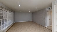 This two-bedroom, one-bathroom single-story home in Houston, TX offers a well-organized layout with tile flooring carried consistently throughout every room. The living room makes a strong first impression with its painted white brick accent wall, recessed lighting, and a sliding glass door that invites natural light while providing outdoor access. A distinctive built-in shelving unit flanks a pass-through opening that connects the living area to the kitchen, adding both character and functionality. The galley-style kitchen is efficiently designed, featuring gray cabinetry, granite-style countertops, a mosaic tile backsplash, black appliances including a refrigerator, electric range, and dishwasher, along with a stainless steel sink. Both bedrooms are comfortably sized, each equipped with a ceiling fan with light fixture and windows fitted with blinds that allow natural light to filter in. The primary bedroom offers a generous footprint with ample wall space. The bathroom is well-appointed with a tiled tub-and-shower combination featuring a decorative mosaic accent stripe, a vanity with granite-style countertops, and tile flooring. Two hallways and two closets contribute to practical storage and circulation throughout the home.