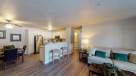 This single-floor unit is thoughtfully designed with a functional, open-concept layout that connects the kitchen, dining, and living areas into one cohesive space. The kitchen is well-appointed with white shaker-style cabinetry, granite-look countertops, and a full suite of stainless steel appliances, including a refrigerator, electric range, and over-the-range microwave. A peninsula with bar seating provides additional workspace and casual dining options. Wood-style flooring runs throughout the main living areas, lending a clean, contemporary feel.

The living room is generously sized and benefits from abundant natural light through a large sliding glass door that opens to a private balcony with outdoor views. A wall-mounted HVAC unit provides climate control in this area.

The unit includes two bedrooms, each with ceiling fans, plush carpeting, and windows that bring in natural light. The primary bedroom offers direct access to an en-suite bathroom. Both bathrooms feature white cabinetry with granite-style countertops and wood-style flooring; one includes a walk-in shower, while the other features a shower-tub combination. Closet storage is present in the bedrooms, completing the practical design of this well-organized unit.
