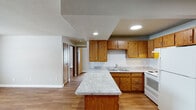 This single-floor residence offers a practical and well-organized layout with consistent warm wood-tone laminate flooring running throughout the entire space. The open-concept kitchen and living area serves as the heart of the home, where a peninsula with granite-look countertops provides both additional prep space and a natural division between cooking and living zones. The kitchen is outfitted with warm oak cabinetry, a classic white subway tile backsplash, a double-basin sink, white appliances including a range and refrigerator, and recessed lighting overhead with a textured ceiling accent above the cooking area. The living area is generously proportioned, offering an open and flexible space for various furniture arrangements. The bedrooms are bright and comfortable, each featuring natural light from gridded windows, baseboard heating, and clean neutral walls. One room also includes a wall-mounted air conditioning unit for added climate control. The full bathroom is neatly appointed with a long white vanity, a tub and shower combination enclosed by sliding glass doors, and wood-look flooring that ties seamlessly to the rest of the home. The overall ambiance is clean, functional, and move-in ready.