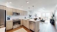 Located at 130 Lake St S in Kirkland, Washington, Unit 413 is a well-designed one-bedroom, one-bathroom residence that makes efficient use of its space through an open-concept layout and modern finishes throughout. Warm hardwood-style flooring runs continuously through the living, dining, and kitchen areas, lending cohesion to the open floor plan.

The kitchen is outfitted with light wood cabinetry, quartz countertops, a white tile backsplash, and stainless steel appliances, including a refrigerator, range, microwave, and dishwasher. A peninsula with bar seating and pendant lighting serves as a natural divider between the kitchen and the combined living and dining area. The living room benefits from large floor-to-ceiling windows and a sliding glass door that opens to a balcony, offering expansive water views.

The bedroom is a well-proportioned retreat with direct access to a dedicated walk-in closet featuring open shelving and hanging storage. The bathroom features light wood vanity cabinetry, a white quartz countertop, a full soaking tub with shower, and hardwood-style flooring that echoes the rest of the unit. The overall ambiance is clean, contemporary, and light-filled.