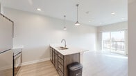 This efficiently designed one-bedroom, one-bathroom unit offers a well-organized single-floor layout that maximizes every square foot. The open-concept kitchen and living area serve as the heart of the unit, anchored by a kitchen peninsula island with a quartz countertop, undermount stainless steel sink, and stylish pendant lighting overhead. The kitchen is equipped with dark wood cabinetry, stainless steel appliances including a refrigerator, electric range, and microwave, providing a fully functional cooking space. Light wood-tone luxury vinyl plank flooring runs throughout the main living areas, complementing the neutral warm-toned walls and creating a bright, clean aesthetic. The living area benefits from a sliding glass door that opens to a private balcony with a metal railing, allowing natural light to fill the space and offering outdoor views. The bedroom features carpeted flooring, a ceiling fan, a dedicated wall-unit HVAC system, and a window with exterior views, creating a comfortable retreat. Two closets provide ample storage throughout the unit. A stacked washer and dryer unit is conveniently tucked within the layout, adding in-unit laundry functionality. The full bathroom includes a single-sink vanity with quartz countertop, dark wood cabinetry, a large mirror, and a tub-shower combination, all finished with consistent light-toned flooring.