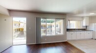 This single-floor unit offers a practical and clean layout designed for comfortable everyday living. The entryway opens into a generous living area finished with rich, dark hardwood flooring that extends throughout the main living spaces. Natural light filters in through a large sliding window overlooking an outdoor courtyard, creating a bright and welcoming atmosphere. A decorative pendant light fixture adds a classic touch near the front entry.

The kitchen is efficiently laid out with white shaker-style cabinetry, dark countertops, light tile flooring, and white appliances including a gas range and full-size refrigerator. A window above the counter provides additional natural light to the workspace.

Multiple bedrooms are accessible from the main living area, each featuring the same warm hardwood flooring, neutral taupe wall tones, and windows that allow in natural light. One bedroom includes a sliding closet, offering convenient built-in storage.

The bathroom is bright and cleanly finished with light tile flooring, a gray vanity with an integrated sink, a framed mirror, and a tub and shower combination accented by patterned tile surround. A frosted window above the tub provides ventilation and privacy. Overall, the unit maintains a clean, neutral palette throughout, offering a versatile canvas for personalization.