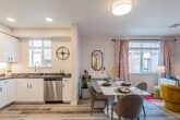 This single-floor residence offers a thoughtfully designed open-concept layout that seamlessly connects the kitchen, dining, and living areas, creating a bright and functional living environment. Light wood-tone flooring runs throughout, providing a cohesive foundation that ties each space together.

The kitchen is well-appointed with white shaker-style cabinetry, dark quartz countertops, stainless steel appliances including a gas range, built-in microwave, and dishwasher, along with under-cabinet lighting. A window above the sink allows natural light to fill the space. The adjacent dining area accommodates a full-sized table and flows naturally into the living room, which features sliding glass doors leading to a private patio with seating.

The bedroom is generously sized, bathed in natural light from a large window, and offers ample closet space. Its neutral palette is complemented by wood-tone flooring and room for a full furniture arrangement. The bathroom includes a full tub-shower combination with clean white tile surround. A dedicated hallway niche houses a stacked full-size washer and dryer, adding practical convenience. Throughout, large windows with plantation-style blinds invite abundant natural light.