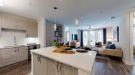 This single-story residence presents a cohesive modern design anchored by an open-concept layout connecting the kitchen, dining, and living areas. The kitchen is outfitted with light wood-grain cabinetry, quartz countertops, a large central island with seating for four, stainless steel appliances including a refrigerator, range, microwave, and dishwasher, and a tile backsplash illuminated by under-cabinet lighting. Pendant lights hang above the island, adding a refined touch. The adjoining living area features wood-look flooring, a ceiling fan, large windows dressed with navy curtains, and a built-in shelving unit, filling the space with natural light and a relaxed, contemporary ambiance.

The two bedrooms each offer generous natural light through large windows with upper transoms, wood-look flooring, and ample space. One bedroom features notably elevated ceilings, enhancing the sense of openness. Both bathrooms echo the unit's modern aesthetic with light wood-grain vanities, quartz countertops, wood-look flooring, and herringbone-patterned runner rugs. The primary bathroom provides access to a walk-in closet with built-in shelving, while the secondary bathroom includes a soaking tub with shower.