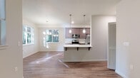 Located at 672 NW Autumncreek Way in Hillsboro, Oregon, this single-floor unit offers a clean, modern aesthetic throughout. The open-concept living and dining area is bright and welcoming, with warm hardwood-style flooring, neutral walls, and multiple windows that frame views of lush surrounding greenery, allowing natural light to fill the space.

The kitchen is a standout feature, designed for both function and style. Rich, dark cabinetry pairs with white countertops and a classic subway tile backsplash. Stainless steel appliances — including a refrigerator, range, and microwave — add a contemporary finish. A peninsula with pendant lighting and bar seating creates an inviting gathering point that connects seamlessly to the living area.

The bedroom is comfortably proportioned with plush carpeting, a large window overlooking the outdoors, and direct access to a closet. Two bathrooms serve the unit: one is a well-appointed full bath featuring a soaking tub and shower combination, dark wood vanity, built-in shelving, and hardwood-style flooring; the other is a compact, efficiently designed half bath with a framed mirror, white vanity, and a natural light source from a side window.

Throughout the unit, textured ceilings, clean white baseboards, and wall-mounted HVAC units contribute to a cohesive, move-in-ready finish. The overall ambiance is bright, tidy, and functional — well-suited for comfortable everyday living.
