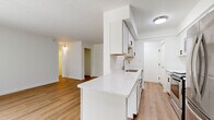 Located at 12000 Fairhill Rd in Cleveland, Ohio, this two-bedroom, one-bathroom unit offers a well-organized layout across a single floor. The galley-style kitchen is thoughtfully designed with white shaker cabinetry featuring matte black hardware, quartz countertops, a stainless steel sink, and a full suite of stainless steel appliances including a refrigerator, electric range, microwave, and dishwasher. The kitchen opens toward a combined living and dining area, which is bright and airy thanks to a large sliding glass door dressed with vertical blinds, allowing generous natural light to fill the space. Warm hardwood-style flooring runs consistently throughout the unit, creating a cohesive and inviting atmosphere. The primary bedroom offers a comfortable footprint with a closet and a window framing natural light, while the second bedroom also includes a closet and its own window. Both rooms are served by baseboard heating. The bathroom is clean and modern, featuring a white vanity with quartz countertop, matte black hardware, and a walk-in shower enclosed by a sleek black-framed glass door. A dedicated entrance and an electrical panel are also present, adding practical functionality to the overall layout.