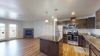 This single-floor residence is designed with an open-concept layout that seamlessly connects the kitchen, dining, and living areas. The kitchen is a standout feature, outfitted with rich, dark-toned cabinetry extending to the upper walls, stainless steel appliances including a gas range, built-in microwave, refrigerator, and dishwasher, and a central island with a dark countertop. Pendant lights hang above the island, complementing recessed ceiling lighting throughout. Warm hardwood-style flooring runs through the main living areas, adding a cohesive, inviting feel.

The living room is generously sized, anchored by a tile-surround fireplace and enhanced by French doors that invite natural light and outdoor views. A dedicated dining area sits adjacent to the kitchen, illuminated by a pendant fixture. The bedrooms feature soft, neutral carpeting and windows that bring in additional natural light.

The bathrooms are finished with wood-toned vanities and light countertops. One bathroom includes a glass-enclosed shower with a sliding door and a window, while another features hardwood-style flooring and a clean, simple layout. The overall aesthetic is modern and cohesive throughout.