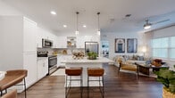 This thoughtfully designed 2-bedroom, 3-bathroom residence offers a cohesive, modern aesthetic across a single floor. Dark hardwood-style flooring flows seamlessly throughout, anchoring the open-concept living area that connects the kitchen, dining, and living spaces. The kitchen is a standout feature, showcasing bright white shaker cabinetry, granite countertops, a subway tile backsplash, stainless steel appliances, and a central island with bar seating illuminated by elegant pendant lighting. The living room is bright and welcoming, with large windows that invite natural light and provide outdoor views. A dedicated dining area comfortably accommodates a dining set alongside the living space. Each bedroom is generously sized, including a spacious primary bedroom, both featuring large windows and continued hardwood-style flooring. The three bathrooms include clean, contemporary finishes, with at least one featuring a glass-enclosed walk-in shower with large-format tile. A dedicated in-unit laundry room with full-size washer and dryer adds everyday convenience. Multiple hallways connect the rooms efficiently, and a closet provides additional storage. The overall ambiance is clean, bright, and modern, with a neutral color palette that enhances the sense of openness throughout.