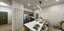 Located at 1818 Fifth Ave in Troy, NY, this contemporary single-floor apartment spans 810 square feet and offers a well-designed layout across multiple rooms. The open-concept kitchen is a standout feature, equipped with stainless steel appliances including a refrigerator, range, and microwave, complemented by warm walnut-toned cabinetry, a white quartz island with a double undermount sink, subway tile backsplash, and modern linear pendant lighting overhead. The living area is bright and inviting, featuring tall ceilings, light hardwood-style flooring, a large window with street views, and recessed lighting. The space accommodates two bedrooms: one with outdoor views through a sizable window and light wood flooring, and another with a dedicated walk-in closet for additional storage. The bathroom includes a tiled floor, a vanity with dark cabinetry, and a shower-tub combination. Throughout the unit, neutral tones and clean lines create a cohesive, modern aesthetic. The unit's efficient floor plan maximizes every square foot, making it a functional and stylish residence in the heart of Troy, New York.