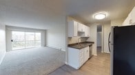This single-floor residential unit offers a practical and comfortable layout designed for everyday living. The open-concept living area is generously proportioned, finished with plush wall-to-wall carpeting and neutral tones throughout. A large sliding glass door floods the space with natural light and provides direct access to a private balcony with outdoor views, making it a bright and inviting area to relax. Baseboard heating runs along the perimeter walls, ensuring year-round comfort.

The kitchen is efficiently designed with white shaker-style cabinetry, dark countertops, a stainless steel sink, a dishwasher, and a full-size refrigerator. Wood-look luxury vinyl plank flooring transitions seamlessly from the kitchen into the hallway, offering durability and easy maintenance in high-traffic areas.

The unit includes two well-sized bedrooms, both carpeted and featuring windows that bring in natural light. One bedroom includes a built-in closet with shelving, providing ample storage. The bathroom is tastefully appointed with a vanity featuring dark countertops, white cabinetry, and wood-look flooring. Textured ceilings are consistent throughout the unit, adding a classic residential finish to the overall aesthetic.