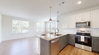 Located at 3355 Club Dr in Lawrenceville, Georgia, this single-floor residence offers a thoughtfully designed open-concept layout filled with natural light and contemporary finishes. The kitchen serves as the heart of the home, showcasing a large central island with granite countertops, a dual-tone cabinet scheme pairing crisp white upper cabinets with gray lower cabinets, stainless steel appliances including a range, microwave, refrigerator, and dishwasher, and stylish pendant lighting overhead. The kitchen flows seamlessly into the living and dining areas, which are bathed in natural light from an abundance of windows offering views of the surrounding greenery. Light-toned hardwood-style flooring extends throughout the main living spaces, complementing the clean, neutral color palette. The bedrooms feature plush carpeting, ceiling fans, and generously sized windows that frame outdoor views, creating a comfortable and airy atmosphere. A well-appointed bathroom includes a tiled tub-shower combination with brushed nickel fixtures and wood-style flooring. The hallway connects the spaces efficiently, with ample storage options nearby. A door off the living area leads to an outdoor deck, further extending the living space and providing scenic outdoor views. The overall ambiance is modern, bright, and move-in ready.