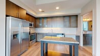 Located in McLean, Virginia, this thoughtfully designed one-bedroom, one-bathroom residence offers a refined modern living experience. Light-toned hardwood flooring flows throughout, complementing the clean, neutral palette that defines the space.

The open-concept kitchen and living area serves as the heart of the home. The kitchen is outfitted with a full suite of stainless steel appliances, including a side-by-side refrigerator, electric range, microwave, and dishwasher. Rich wood upper cabinetry with glass-front panels is paired with sleek gray lower cabinets and granite countertops. A movable island with a matching granite surface and under-lit base adds both functionality and style.

The living area is bathed in natural light from expansive floor-to-ceiling windows that frame sweeping views of the surrounding McLean skyline and lush treetops. A sliding glass door provides access to a private balcony, extending the living space outdoors.

The bedroom is a well-proportioned retreat featuring its own large windows with outdoor views and direct access to a dedicated walk-in closet with built-in shelving. The bathroom is finished with large-format tile flooring, a granite-topped vanity with gray cabinetry, and a soaking tub with tiled surround. A connecting hallway with louvered closet doors completes this well-appointed residence.