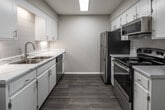 This single-floor residence offers a thoughtfully updated interior with a clean, modern aesthetic throughout. The galley-style kitchen is a standout feature, showcasing crisp white cabinetry, marble-look countertops, a subway tile backsplash, and wood-look luxury vinyl flooring. Stainless steel appliances — including a refrigerator, electric range, over-the-range microwave, and dishwasher — are neatly arranged along both sides of the kitchen, maximizing efficiency. A large overhead skylight-style flush light keeps the space well-illuminated.

Adjacent to the kitchen, the open living area continues the wood-look flooring and is bathed in natural light from a large window, creating a bright and welcoming atmosphere. An in-unit washer is conveniently located at the edge of this space, adding practical everyday functionality.

The bedrooms offer a comfortable retreat, with one room featuring plush carpeting, a ceiling fan with light fixture, and a window that lets in natural light. Another bedroom continues the wood-look flooring and includes a wide window dressed with horizontal blinds.

The bathroom is finished with a clean, all-white tub and shower surround equipped with brushed nickel fixtures, maintaining the home's consistent, refreshed aesthetic throughout.