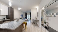 Located at 5110 S Manhattan Ave in Tampa, Florida, this single-floor residence showcases a thoughtfully designed open-concept layout with modern finishes throughout. Light wood-style flooring flows seamlessly through the main living areas, creating a bright and cohesive aesthetic.

The kitchen is a standout feature, boasting granite countertops, a large center island with bar seating, two-tone cabinetry — crisp white uppers paired with dark wood lowers — a subway tile backsplash, and a full suite of stainless steel appliances. Pendant lighting adds a refined touch overhead.

The open living area is generous and welcoming, with large sliding glass doors that invite natural light and provide outdoor access. A ceiling fan, dedicated workspace with a granite-topped built-in desk, and a smooth transition from dining to lounge areas make the layout both functional and comfortable.

The bedrooms feature plush carpeting, large windows with draping curtains, and ample space for rest and storage. The bathroom is well-finished with granite vanity countertops, dark wood cabinetry, a tub-shower combination, and light tile flooring that continues the home's clean, contemporary theme throughout.