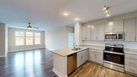 Located at 5101 Attain Centre Dr in Fredericksburg, VA, this well-appointed one-bedroom, one-bathroom residence offers a thoughtfully designed open-concept layout. The kitchen serves as a centerpiece of the living space, showcasing granite countertops, gray shaker-style cabinetry, a peninsula with an undermount sink, and a full suite of stainless steel appliances including a refrigerator, range, microwave, and dishwasher. A white tile backsplash and recessed lighting complete the kitchen's clean, modern aesthetic. The kitchen flows seamlessly into the living room, which features hardwood-style flooring, neutral-toned walls, a ceiling fan, and a large window that invites abundant natural light and outdoor views. The bedroom is carpeted for comfort, with soft neutral walls and a generous walk-in closet outfitted with multi-tier wire shelving for ample storage. The bathroom offers a double-sink vanity with granite countertops, gray cabinetry, brushed nickel hardware, a large mirror with overhead lighting, and a tub-shower combination. Throughout the residence, consistent use of hardwood-style flooring, neutral tones, and modern finishes creates a cohesive and inviting atmosphere.