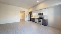 Located at 1905 Concord Blvd in Concord, California, this single-floor unit offers a thoughtfully designed open-concept layout that maximizes functionality within a compact footprint. Light-toned luxury vinyl plank flooring flows throughout the main living area, reflecting natural light and lending the space a clean, modern aesthetic. A hallway entry with textured walls leads into the main living area, which features large windows that invite ample natural light and offer views of the surrounding greenery and a private balcony beyond sliding glass doors.

The kitchen is a standout feature, designed with a sleek two-tone cabinet scheme pairing dark espresso lower cabinets with crisp white upper cabinetry. A full suite of stainless steel appliances — including a refrigerator, electric range, dishwasher, and microwave — complement the light countertops and tile backsplash. Recessed lighting above provides a bright, functional workspace.

The bathroom is finished with large-format light tile flooring and features a dark-toned vanity with a white countertop, an overhead wall-mounted cabinet, a well-lit mirror, and accessibility-ready grab bars in the shower area. A dedicated closet provides organized storage. The overall palette of warm neutrals and modern finishes creates a cohesive, move-in-ready environment.