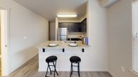 This two-floor residence offers a functional and well-designed layout with a neutral color palette throughout. The kitchen is a standout feature, equipped with dark cabinetry, stainless steel appliances including a refrigerator, range, and built-in microwave, and light granite-style countertops. A peninsula with bar seating provides a casual dining option, seamlessly connecting the kitchen to the living area. Light wood-style flooring runs through the main living spaces, contributing to a clean, modern aesthetic.

The bedrooms are carpeted for comfort and receive natural light through windows fitted with horizontal blinds. At least one bedroom includes a walk-in closet with built-in shelving and hanging rods. The space also features angled ceilings in certain areas, adding architectural interest.

Multiple bathrooms are present, each with tiled flooring, a toilet, vanity with cabinetry, and a tub-shower combination. A dedicated laundry area with side-by-side appliance connections is also included. The overall layout, as seen in the overhead floor plan view, presents a spacious and efficiently organized interior across both levels.