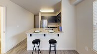 This two-floor residence offers a functional and well-designed layout with a neutral color palette throughout. The kitchen is a standout feature, equipped with dark cabinetry, stainless steel appliances including a refrigerator, range, and built-in microwave, and light granite-style countertops. A peninsula with bar seating provides a casual dining option, seamlessly connecting the kitchen to the living area. Light wood-style flooring runs through the main living spaces, contributing to a clean, modern aesthetic.

The bedrooms are carpeted for comfort and receive natural light through windows fitted with horizontal blinds. At least one bedroom includes a walk-in closet with built-in shelving and hanging rods. The space also features angled ceilings in certain areas, adding architectural interest.

Multiple bathrooms are present, each with tiled flooring, a toilet, vanity with cabinetry, and a tub-shower combination. A dedicated laundry area with side-by-side appliance connections is also included. The overall layout, as seen in the overhead floor plan view, presents a spacious and efficiently organized interior across both levels.
