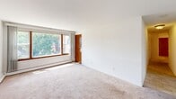 Located at 6946 W 65th St in Chicago, IL, this single-floor unit offers three bedrooms and one bathroom within a compact, efficiently arranged floor plan. The layout, visible in the dollhouse view, organizes the rooms in a connected configuration with warm-toned wooden doors throughout, providing a cohesive aesthetic.

The spacious primary bedroom is the standout space of the unit, offering generous room for furnishings, neutral carpet flooring, a ceiling fan with light fixture, and a double-door closet. The remaining bedrooms are similarly finished with plush carpeting, ceiling fans, and windows framing views of the surrounding Chicago neighborhood. Baseboard heating runs along the walls in multiple rooms, ensuring efficient climate control, while a wall-mounted air conditioning unit provides cooling in one of the bedrooms.

The full bathroom is tiled throughout, featuring earthy, neutral-toned tile work in the shower/tub surround and light tile flooring. A wood-finish vanity and a textured ceiling complete the functional space.

A large picture window in what appears to be the main living or primary area allows abundant natural light to fill the room, creating a bright and open feel. Throughout the unit, clean white walls and consistent warm wood accents on doors and trim contribute to a simple, practical interior character well-suited for comfortable everyday living.
