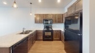 Located at 5501 E 18th St in Sioux Falls, South Dakota, this single-floor unit offers a well-designed, open-concept layout with a clean, modern aesthetic throughout. The kitchen is a standout feature, showcasing rich dark wood cabinetry, light marble-style countertops, and a full suite of black appliances including a range, over-the-range microwave, dishwasher, and refrigerator. A peninsula with an undermount sink and pendant lighting creates a natural divide between the kitchen and the open living area, making the space feel connected yet purposeful. Light wood-style flooring runs throughout the main living areas, adding warmth and continuity.

The living area benefits from natural light through a large window with exterior views of the surrounding neighborhood. The bedroom features plush carpeting, a bright window, and a generous walk-in closet with built-in wire shelving. An additional closet with double doors provides further storage flexibility. Two bathrooms are finished with matching dark wood vanities, marble-style countertops, and wood-look flooring. One bathroom includes a tub/shower combination. An in-unit laundry area adds everyday convenience, completing this thoughtfully laid-out single-floor residence.