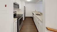Located at 103 9th Street in Boston's Charlestown neighborhood, this single-floor residence offers a clean, modern interior designed for comfortable urban living. Rich, dark hardwood flooring runs consistently throughout the space, providing a warm and cohesive aesthetic from room to room.

The galley-style kitchen is efficiently laid out with white shaker cabinetry, light quartz countertops, and a full suite of stainless steel appliances, including an electric range with overhead microwave, refrigerator, and dishwasher. A stainless steel undermount sink completes the functional and polished kitchen design.

The living areas are generously sized, featuring crisp white walls and large windows that invite natural light and offer street-level views of the surrounding neighborhood. The open layout provides flexibility for a variety of furniture arrangements, and subtle stepped transitions between areas add architectural interest to the floor plan.

The bedroom is a well-proportioned, sunlit room with a large window framing views of nearby trees and the streetscape, creating a bright and airy retreat. Storage is available via a closet visible from the living area.

The bathroom is finished with classic white tile in the tub/shower surround, neutral tile flooring, and a clean white vanity, delivering a timeless and functional design. Overall, this residence combines practical layout with consistent modern finishes throughout.