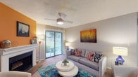 This single-floor apartment at River Oak Apartments offers a thoughtfully designed layout with a comfortable flow between living, sleeping, and functional spaces. The living room serves as the centerpiece of the home, highlighted by a wood-burning fireplace set against a bold accent wall. A ceiling fan overhead and sliding glass doors lead to a private patio, filling the room with natural light and outdoor views. Carpeted flooring and a textured ceiling complete the relaxed atmosphere.

The galley-style kitchen features dark cabinetry with brushed nickel hardware, light stone-patterned countertops, stainless steel appliances, and wood-look flooring. A doorway connects the kitchen to an adjacent utility or pantry space, adding practical convenience.

Both bedrooms are carpeted and receive natural light through windows fitted with blinds and decorative curtains. Each room offers generous space for furnishings, and at least one bedroom includes a walk-in closet with wire shelving. The bathroom presents a clean, neutral aesthetic with dark vanity cabinetry, white countertops, and wood-look flooring, contributing to a cohesive design throughout the apartment.