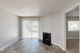 Located near the Cherry Creek Trail in Denver, CO, this efficient one-bedroom, one-bathroom unit is thoughtfully laid out across a single floor. The living room serves as the focal point of the space, featuring durable wood-look plank flooring, a classic tile-surround fireplace, and a full-length sliding glass door with vertical blinds that invites natural light and provides outdoor access. The neutral gray walls and textured ceiling create a clean, understated aesthetic throughout. The kitchen is efficiently designed with a peninsula breakfast bar, white cabinetry, matching white appliances, and light wood-look flooring that extends through the common areas, making the space feel cohesive and open. Recessed lighting illuminates the kitchen and hallway areas. The bedroom offers plush carpeting underfoot, a closet, and a window with horizontal blinds that frames views of surrounding greenery, providing a calm and restful environment. The bathroom is finished with rich wood-tone flooring, a white vanity with brushed nickel hardware, a toilet, and a tub-shower combination. Clean white trim and consistent neutral tones tie all rooms together, resulting in a move-in ready unit with a modern, practical character well-suited to its Denver location.