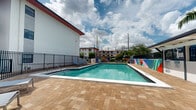 Located in Hialeah, Florida, this outdoor pool area offers a well-appointed recreational space designed for relaxation and leisure. The centerpiece is a generously sized rectangular swimming pool filled with clear, turquoise water, framed by a durable paver deck that provides ample space for lounging and socializing.

Surrounding the pool, a collection of modern chaise lounges and patio seating invites guests to unwind under the South Florida sun. A standout feature of the space is a bold, colorful mural adorning one of the perimeter walls, adding a vibrant artistic element that enlivens the outdoor environment. A covered pergola-style structure along one side of the deck offers shaded seating, ideal for those seeking relief from the sun.

The pool area is enclosed by a black metal security fence, ensuring safety and privacy. A distinctive blue structural tower, visible from the pool deck, adds a striking architectural accent to the space. Mature palm trees and tropical greenery are positioned throughout the perimeter, reinforcing the Florida ambiance and providing natural shade.

The multi-story building that wraps around the courtyard features balconies that overlook the pool, creating an open, resort-like atmosphere. The combination of colorful design elements, lush landscaping, and thoughtful amenities makes this pool area a vibrant and functional outdoor retreat.