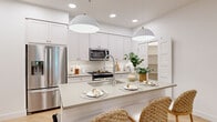 This well-appointed 2-bedroom, 2-bathroom residence offers a seamlessly flowing single-floor layout designed for comfortable, modern living. The open-concept kitchen and living area serves as the heart of the home, showcasing white shaker cabinetry with gold hardware, stainless steel appliances, a subway tile backsplash, and a central island with a undermount sink and pendant lighting — ideal for both casual dining and entertaining. Light wood-tone flooring runs throughout, complementing the crisp white walls and recessed lighting that lend the space a bright, airy feel.

The living room is generously proportioned, featuring a ceiling fan, large windows, and access to an outdoor balcony that invites natural light to pour in. The primary bedroom is a serene retreat with large windows framing outdoor views and ample closet space. The second bedroom continues the warm, understated aesthetic with wood flooring and a sliding barn-style door. Both bathrooms are clean and contemporary, with one featuring a full soaking tub with white subway tile surround. Additional highlights include a dedicated laundry room with a full-size Whirlpool washer and dryer, two closets for generous storage, and a cohesive neutral palette throughout that creates a calm, inviting ambiance.
