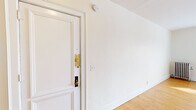 This single-floor residence offers two bedrooms and one bathroom within a efficiently arranged layout. Throughout the living areas and bedrooms, warm-toned hardwood floors add character and a sense of continuity. The entry area features crisp white walls and clean white trim, with a classic paneled door fitted with brass hardware that sets a timeless tone from the moment you step inside.

The spacious primary bedroom is notably generous, filled with natural light streaming through multiple windows dressed with horizontal blinds. A cast-iron radiator provides classic charm while offering reliable in-unit heating. A ceiling fan with lighting anchors the room, and two white panel doors — one leading to a closet and another to the hallway — add functional convenience.

The second bedroom is similarly bright, with windows on two walls inviting ample daylight and a ceiling fan overhead, along with its own radiator for comfort.

The bathroom retains vintage character with classic white hexagonal tile flooring, white subway-tiled walls, a pedestal sink, and a wall-mounted sconce beside a framed mirror. A window with blinds provides natural light and ventilation, completing the clean, timeless aesthetic of this well-preserved space.